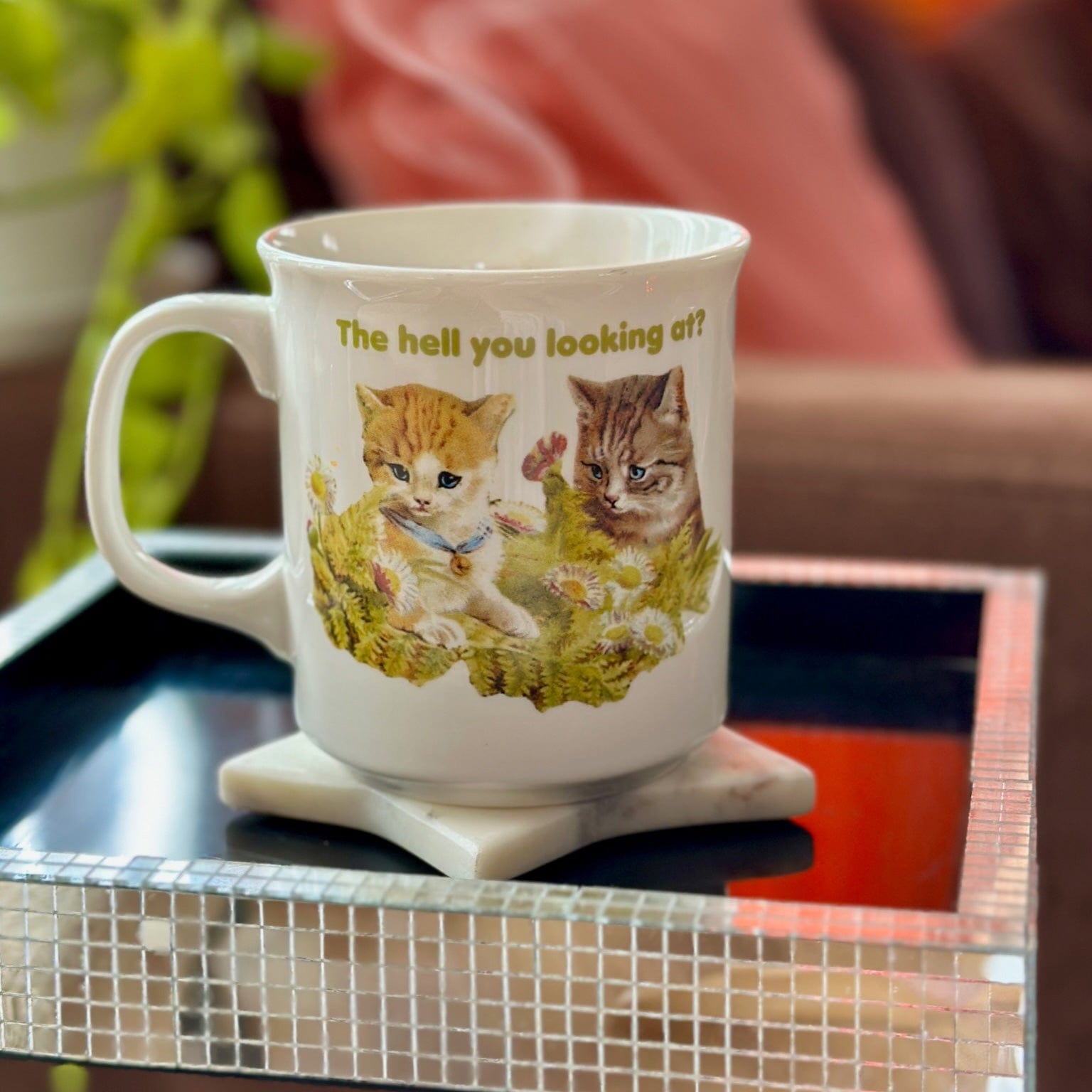 A mug that says "the hell you looking at?" on a side table