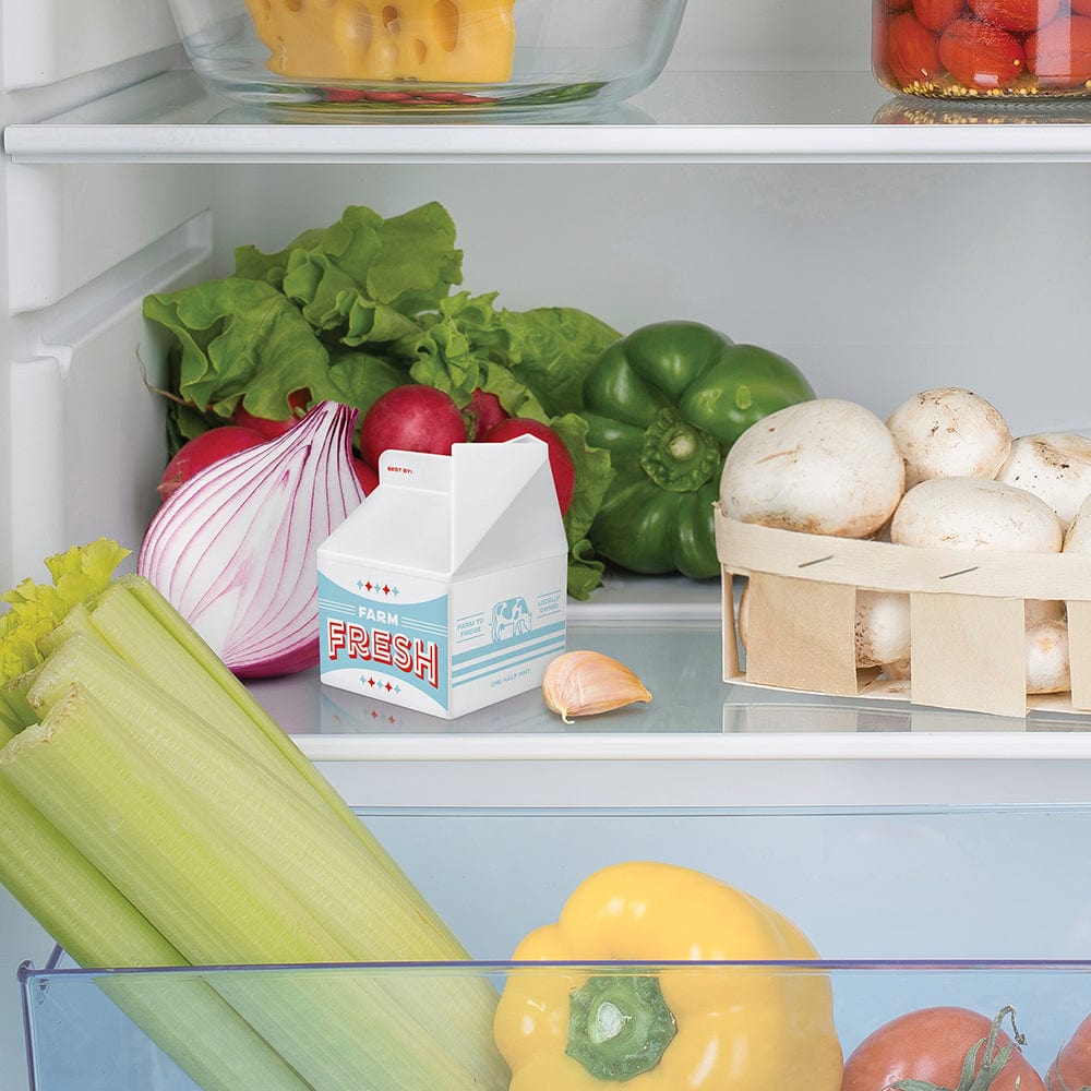 A plastic milk carton odor absorber in a refrigerator surrounded by onions, peppers, mushrooms, celery, garlic, and lettuce.