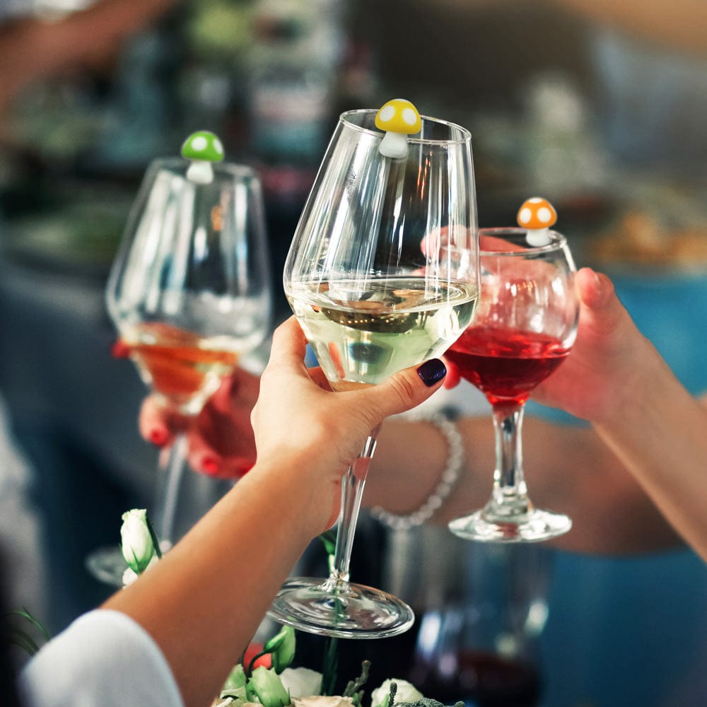 Three people at a party clicking wine glasses with small mushroom drink markers attached.